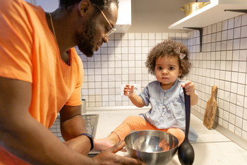 African dad with a little daughter standing in the kitchen preparing to eat for mom. Day off for mom