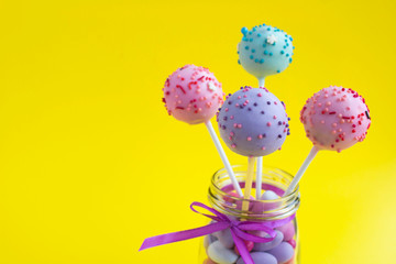 Different cake pops in the glass jar on the yellow background. Copy space. Closeup.