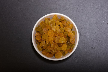 Raisins in white bowl on the black stone plate