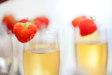 Close up of glasses of sparkling wine or champagne and strawberry on a blurry background during some sort of festivity or celebration such as a wedding, borthday or newyear