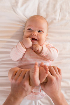 Newborn Baby Lying On The Bed, Dad Holding The Baby's Legs With His Hands Top View. Vrtical Photography