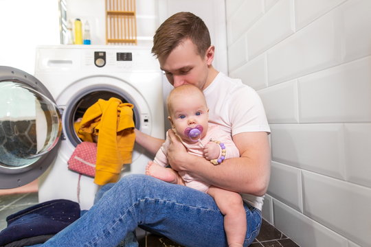 Gender Equality. Dad With A Baby Sitting In A Laundress Washing Dirty Things In A Washing Machine