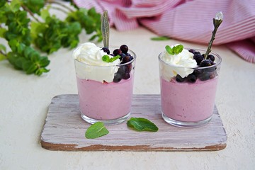 Dessert, airy mousse whipped cream and mashed black currants or pudding in portion jars on light blue background. Decorated with frozen black currants and fresh mint. Dessert on Valentine Day.