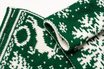 Fototapeta premium Fragment of a beautiful green scarf with white drawings depicting deer, spruce and snowflakes