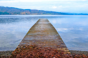 A long wooden jetty on a lake, looking out over a clear calm blue lake, winderemere, England,