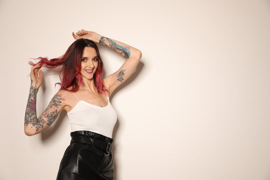 Beautiful woman with tattoos on arms against light background. Space for text