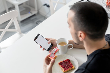 The guy watches the news on the phone during breakfast