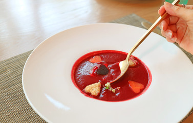 Female's Hand Scooping Beetroot Soup with Heart Shaped Vegetables in White Plate