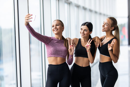 Selfie time, girls. Three girlfriends in fashionable sport outfits are posing for a selfie photo at gym