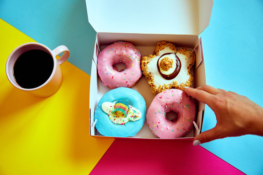 Sprinkled donuts in box and cup of coffee on colorful background.