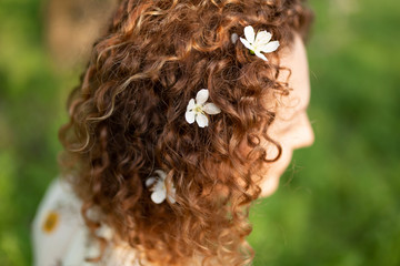 Attractive young woman with white flowers woven in her curly hair. Spring fashion concept