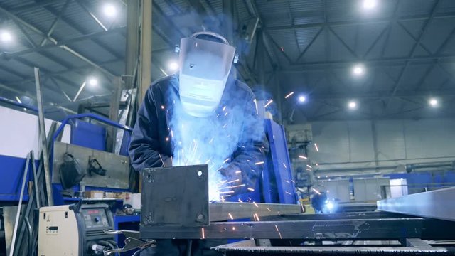 Male welder in a protective mask is processing metal. Professional Heavy Industry Welder working at factory facility.
