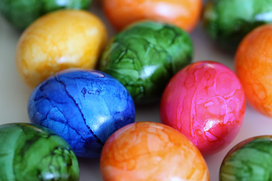 Colorful and joyful Easter decorations on a table. Closeup color image of multiple painted Easter eggs with happy and vibrant colors including blue, green, orange, yellow and pink. Shiny marbled color