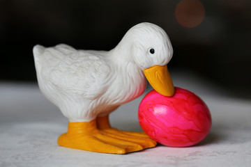 Colorful and joyful Easter decorations on a table. Closeup color image of one ceramic white Easter duck figure and colorful painted Easter eggs with shiny marbled surface. Happy and vibrant colors.