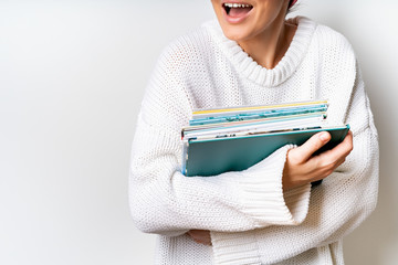Woman in white woolen sweater holding a stack of children's books in hands. Free space for your mock up of reading book concept background.