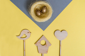 Holiday decoration. Easter egg gold colors. Yellow background, gray napkin. Wooden chicken, easter bunny on a stick.Flat lay, top view, trendy modern celebration style