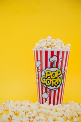 Butter popcorn in a red popcorn cup, snack in the house or cinema on a yellow background