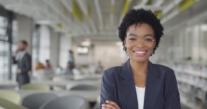Successful millennial businesswoman in suit smiling and turning head to camera.Young african american female leader office worker standing in modern office. Portraits