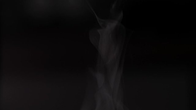 Trickle of Steam Slowly Rising from the Cup. White steam rises light, graceful twists on a black background