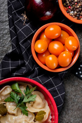 Small yellow cherry tomatoes in ceramic bowl on gray stone background. Cherry tomatoes and tasty dumplings pelmeni meat. Close up.