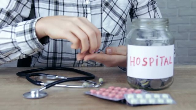 Woman drops some loose change into a saving jar, which has Hospital written on it