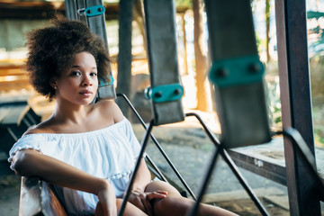 Portrait of beautiful happy young woman with afro sitting on bench swing 