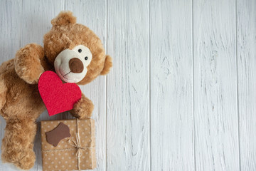 Greeting card for birthday, mother's day, Valentine's day. Toy bear with hearts, gift boxes on a light wooden background. View from above