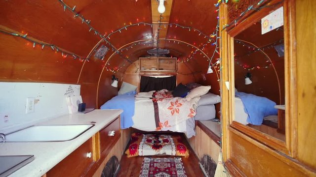 Interior of a cozy camper van. Colorful fairy lights are strung from the wood paneled ceiling over the bed on the camp trailer. Shot shows nontraditional vacation rental and freedom of van dwelling.