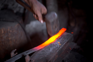 Blacksmith's hands at work. In one hand a hammer, in the other a workpiece of hot metal. Master methodically hammer hits the anvil. An example of the hard work of ancient crafts.