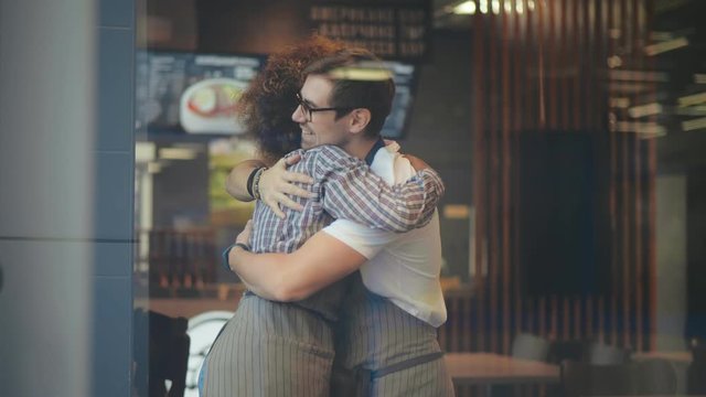 Multicultural waiters giving each other high-five and hugging in cafeteria