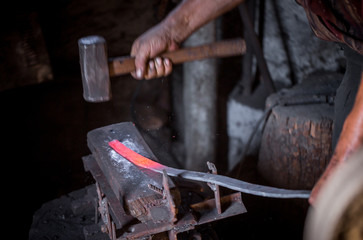 Blacksmith's hands at work. In one hand a hammer, in the other a workpiece of hot metal. Master methodically hammer hits the anvil. An example of the hard work of ancient crafts.