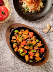 Delicious oven-baked potatoes with herbs and vegetables in a pan, rustic style. Potatoes fried, red cherry tomato, zucchini, onion on gray stone background.