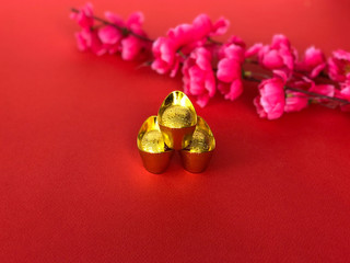 Chinese New Year concept. Golden ingots and chinese cherry blossom flower on red background. The Chinese words written on the top of the ingots literally means ?lucky fortune?.