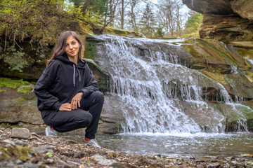 Young girl hiker near small waterfall at mountains. Woman enjoy and relax at nature