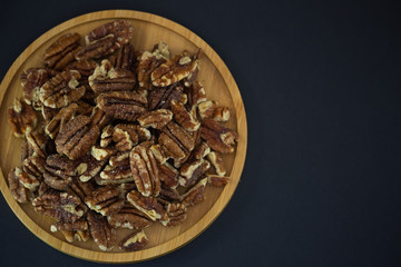 pecan nut or Pekannuss nuts group Protein and healthy food for diet in a wooden plate on a black background.
