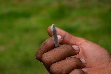 Homemade cigarette held by the hand of a black man and dirty hands. Poverty and drug addiction concept. Marijuana in cigarette.