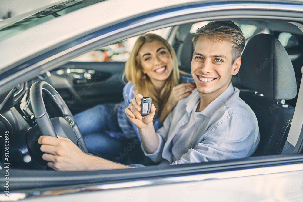 Wall mural happy couple holding a car key after buying it in showroom.