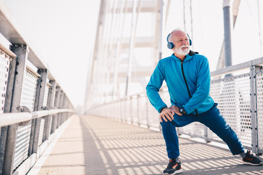 An Elderly Man Stretching Outdoors And Wearing Headphones.