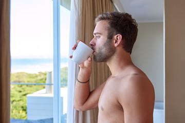 Man sipping morning coffee with view of beach through window