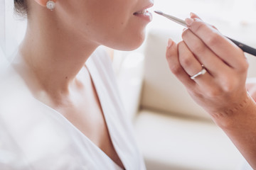 Makeup artist paints lips of a beautiful bride. Tender morning of the bride. young girl paints lips with a brush in a gentle shade.