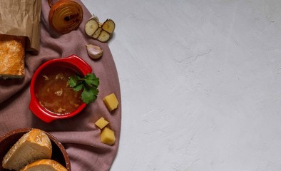 onion soup in a red pot and baguette in a paper bag, baked vegetables and cheese on a purple cloth, top view