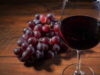 Glass of red wine in focus, cluster of fresh red grapes on a wooden table out of focus, top view.