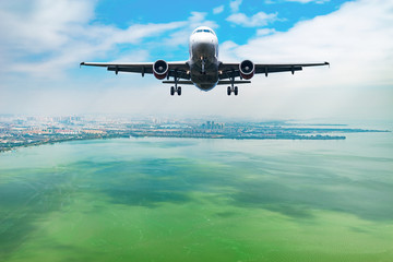 Flight of the passenger plane above the lake by the city.