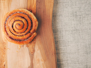 One traditional freshly cooked cinnamon swirl, pastry product on a wooden board surface and simple table cloth. Close up.