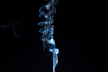 Puff of smoke from an incense stick on a dark background.