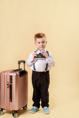 Little boy sitting on suitcases, preparing for the holiday. Business boy, cheerful active child. Globe, old vintage camera and travel suitcase. In the studio on a light background.