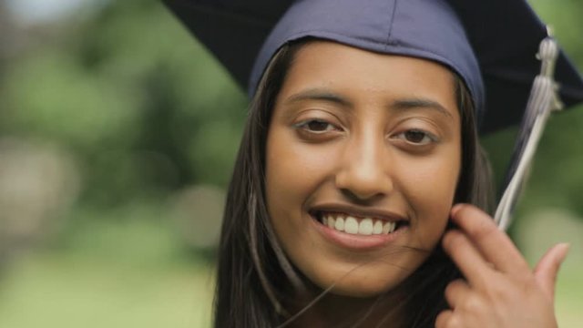 Portrait of a confident and happy young Indian woman smiling and wearing her high school graduation cap and gown