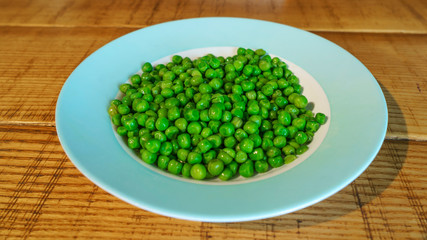 Fresh green peas in earthenware plate on wooden background, top view. Rustic table background