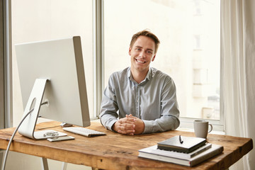 Smiling young professional sitting at his desk in a bright office