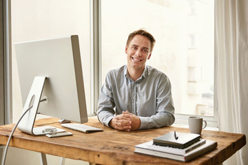 Fototapeta premium Smiling young professional sitting at his desk in a bright office